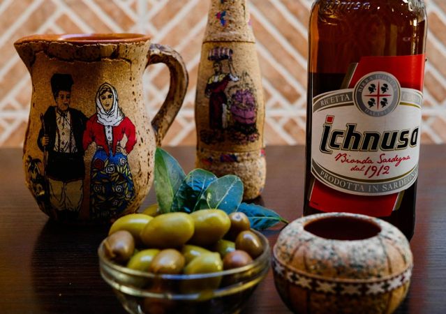 Brocca in ceramica sarda, birra Ichnusa e olive sul tavolo, vicino al Colosseo