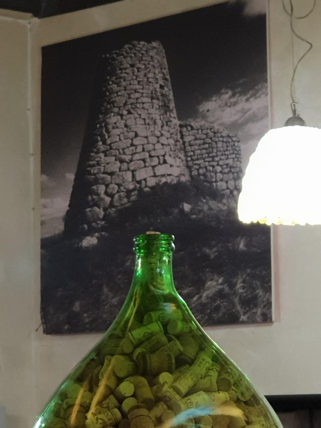 Damigiana verde davanti alla foto di un nuraghe sardo, vicino al Colosseo